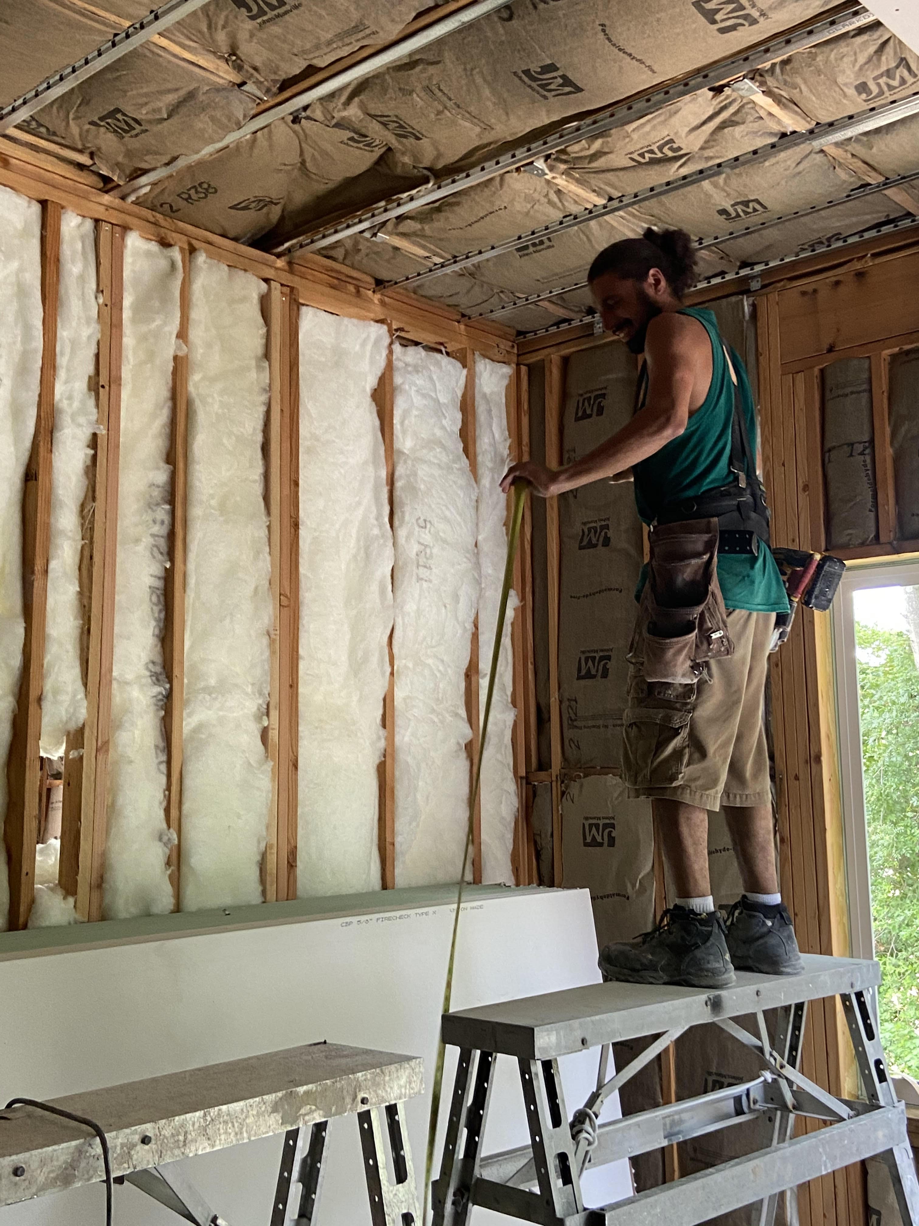 worker measuring insulation with paperbacked Johns Manville in back
