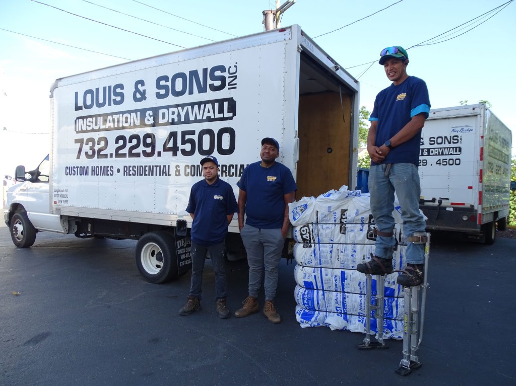 Three workers standing near Louis and Sons box truck. One worker is on stilts with insulation behind him.